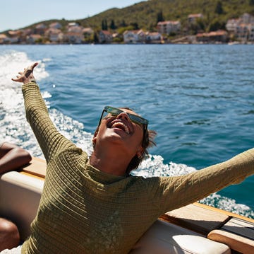 happy young woman with arms raised in motorboat enjoying sunny day